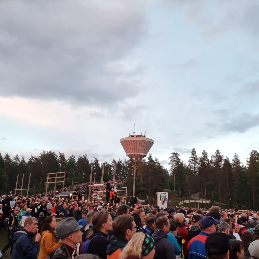 Jukolan ykkösosuuden iltalähtö. Koko lähtöalue täynnä ihmisiä katsomassa iltahämärässä. Taustalla Mynämäen vesitorni.
