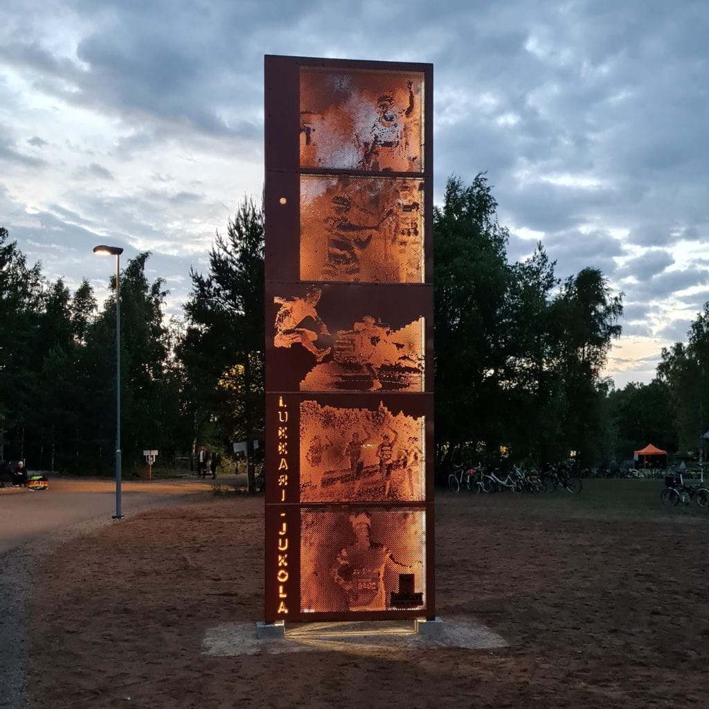 Jukolan metallinen korkea sisääntuloportti valaistuna iltahämärässä.
