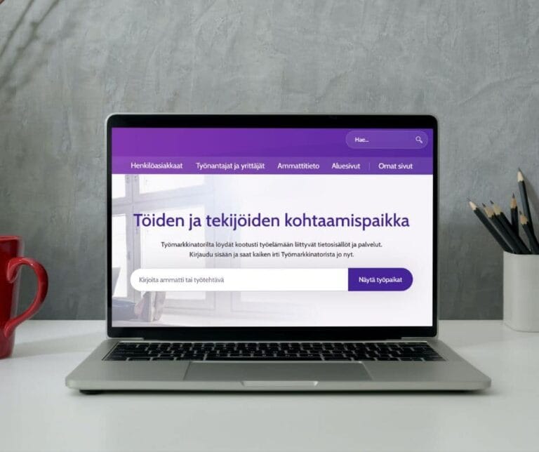 Kannattevan tietokoneen näyttö, jossa on Työmarkkinatorin verkkosivut auki. Taustalle harmaa seinä ja pöydällä kyniä ja kahvikuppi.