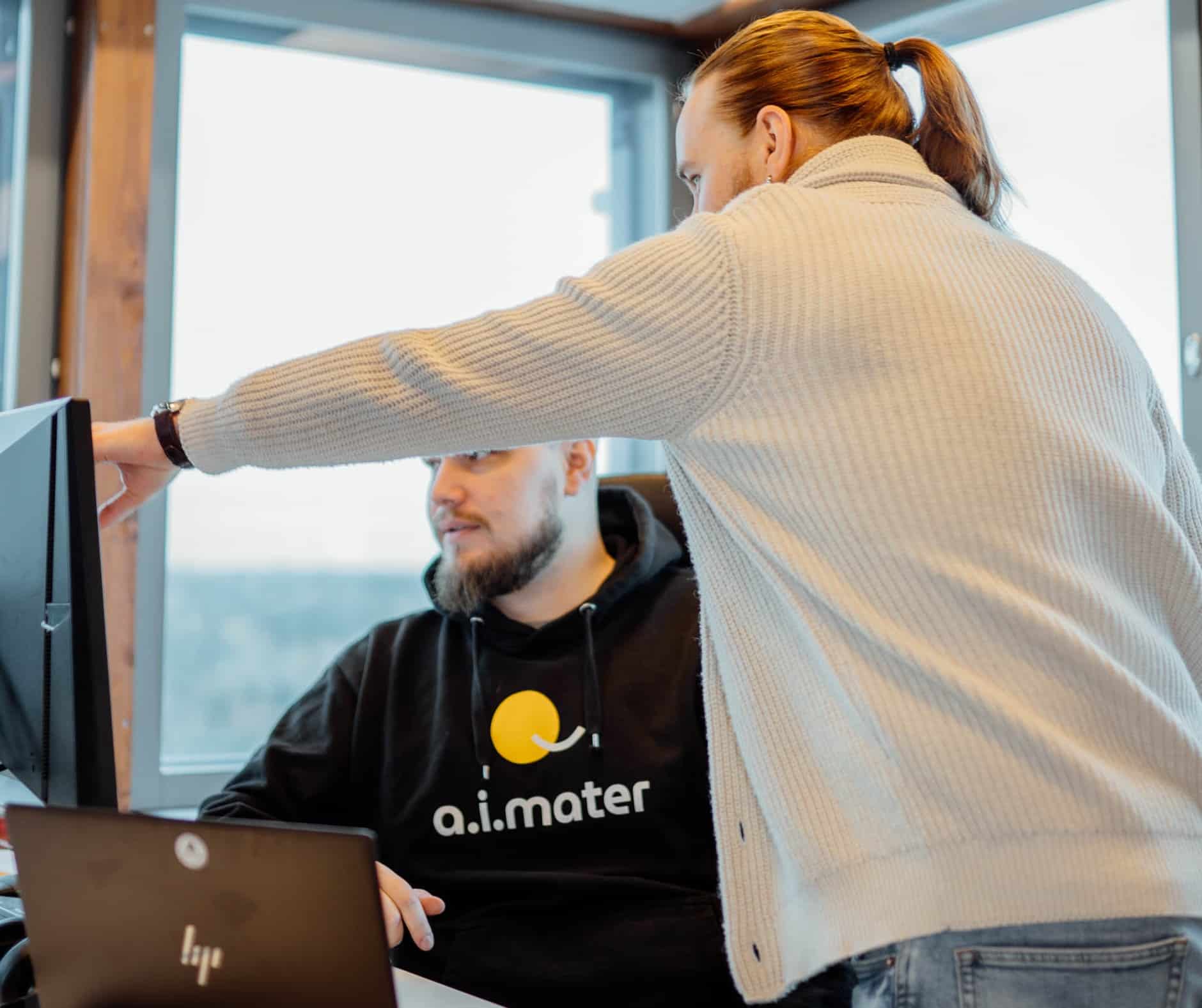 Aimaterin työntekijät Roope ja Niko tutkivat työpöydän edessä tietokoneelta jotain. Roope juuri osoittaa kädellään näyttöä.