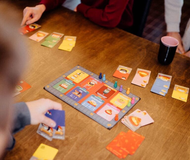 Pöydälle on levitetty Sushi go lautapeli. Kuvan reunoilla näkyy työntekijöiden käsiä, jotka pelaavat peliä.